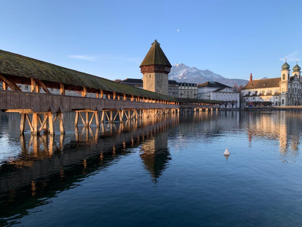 Picturesque scenery of famous ancient Chapel Bridge with water tower crossing river against cloudless blue sky in Lucerne