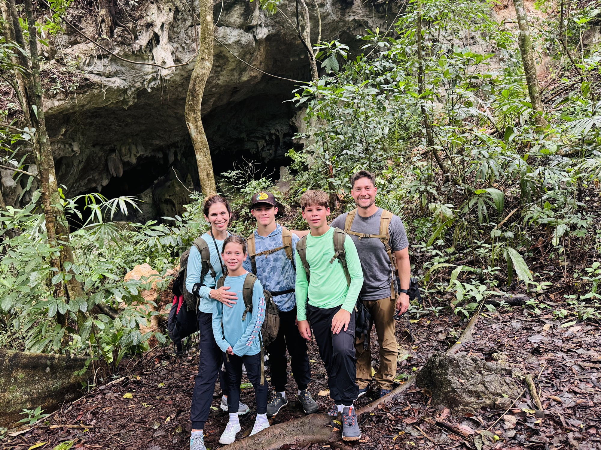Family hiking to Belize waterfall cave entrance with headlamps and harnesses